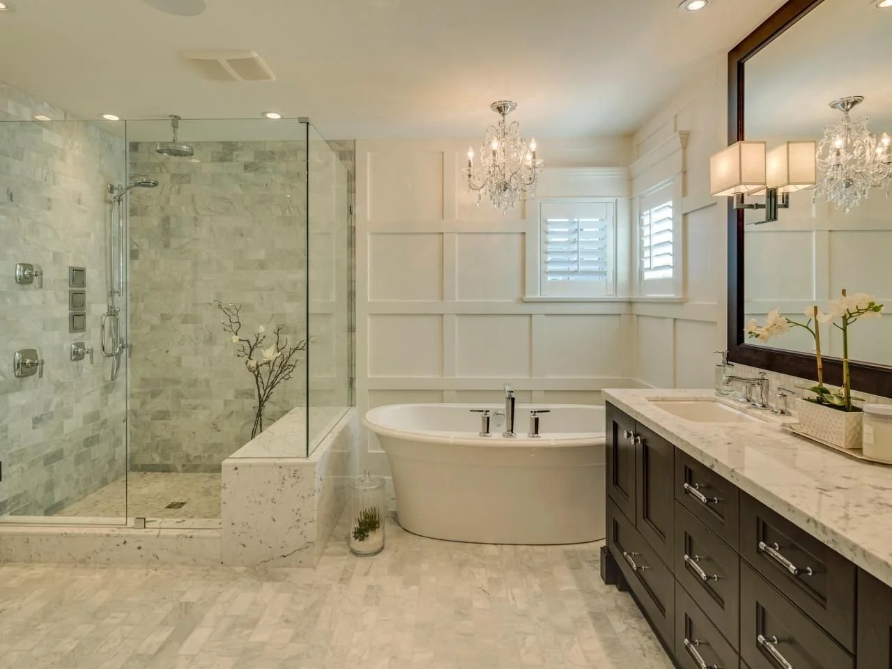 Marble tiled walk-in shower beside a freestanding tub and dark double vanity in a bathroom remodeled by Decoriam