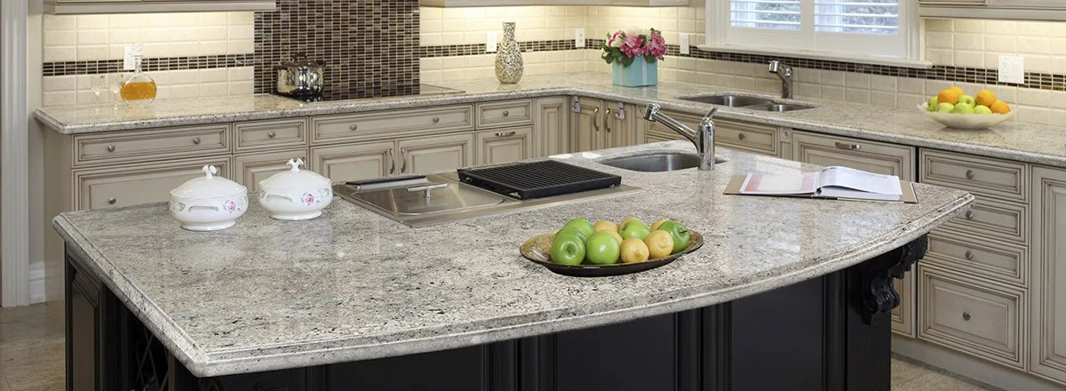 Speckled white granite countertop running across a kitchen island and perimeter cabinets, fabricated by Decoriam