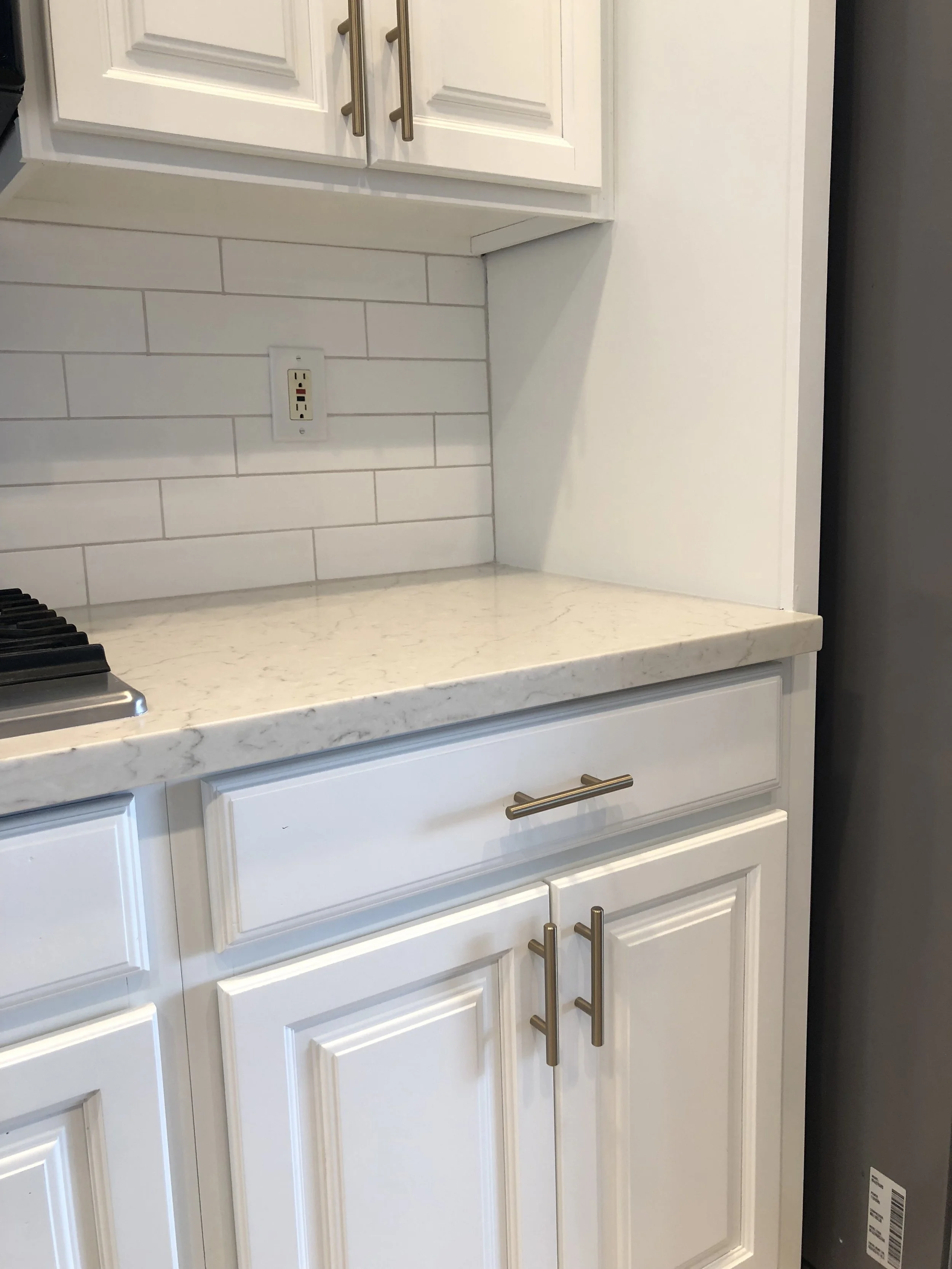 Detail of white cabinetry with brass pulls and a veined quartz countertop