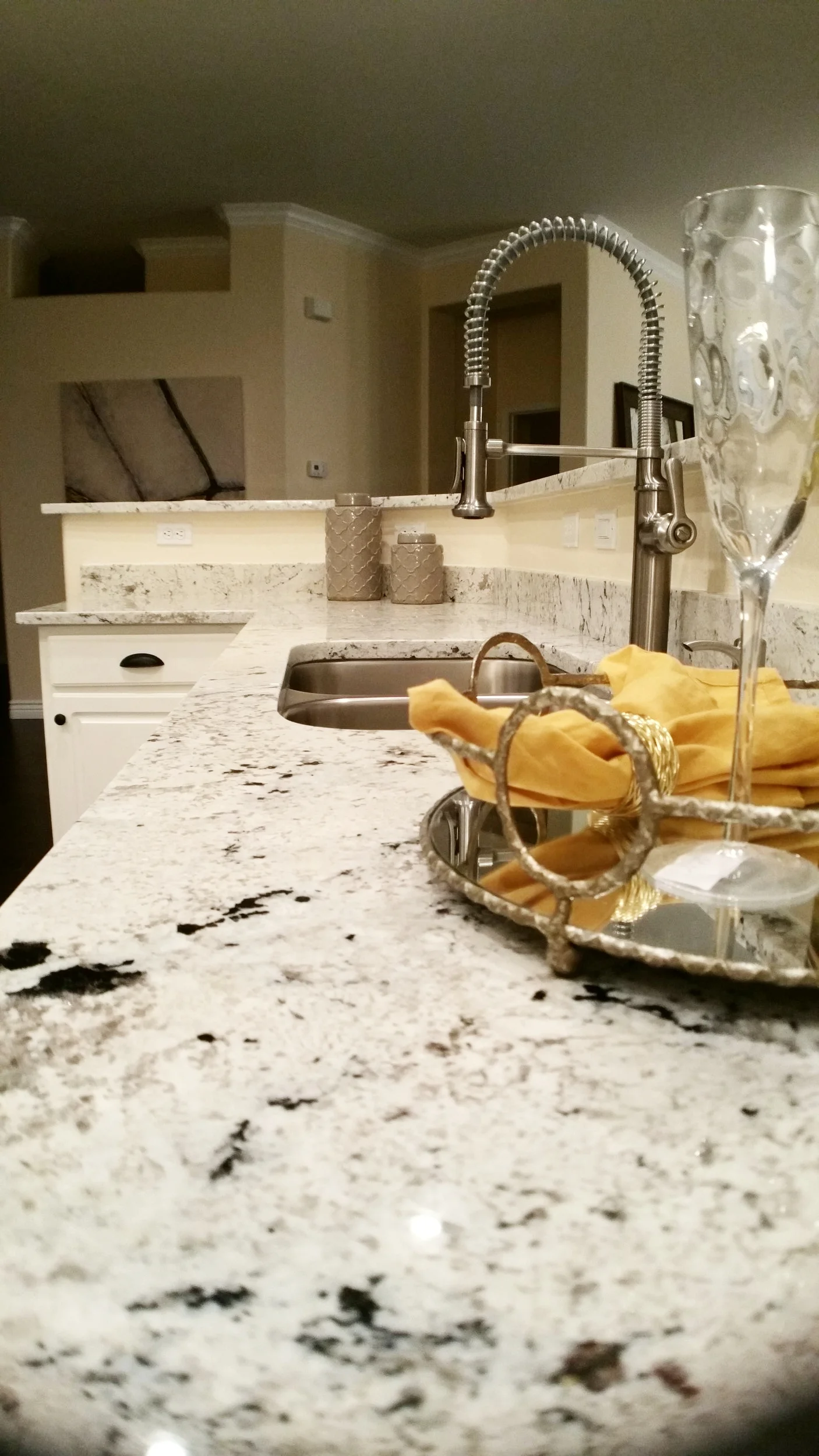 Speckled white and black granite countertop running along a cream kitchen peninsula with a stainless pull-down faucet