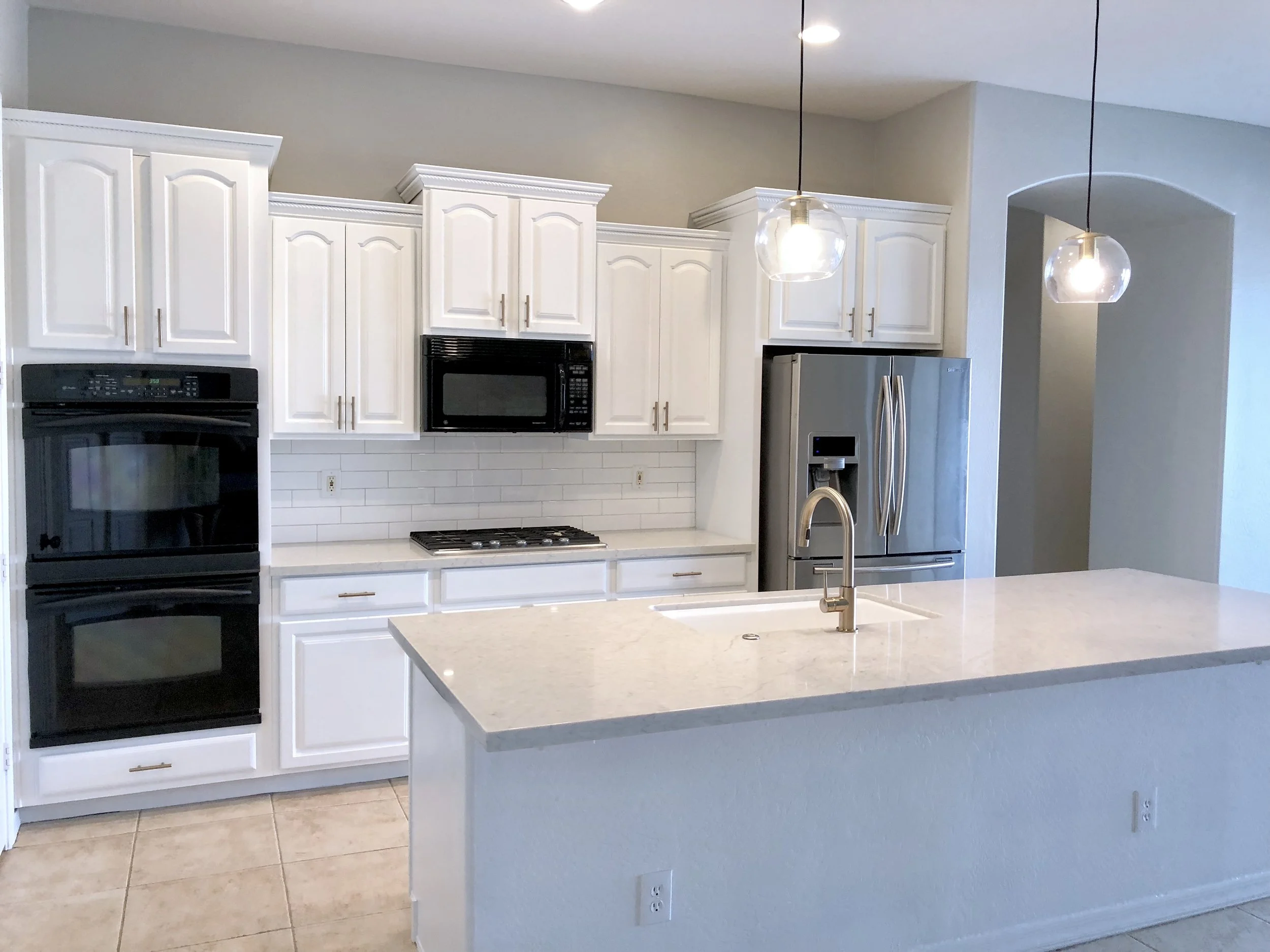 White shaker kitchen with a quartz waterfall island and brushed nickel fixtures, remodeled by Decoriam